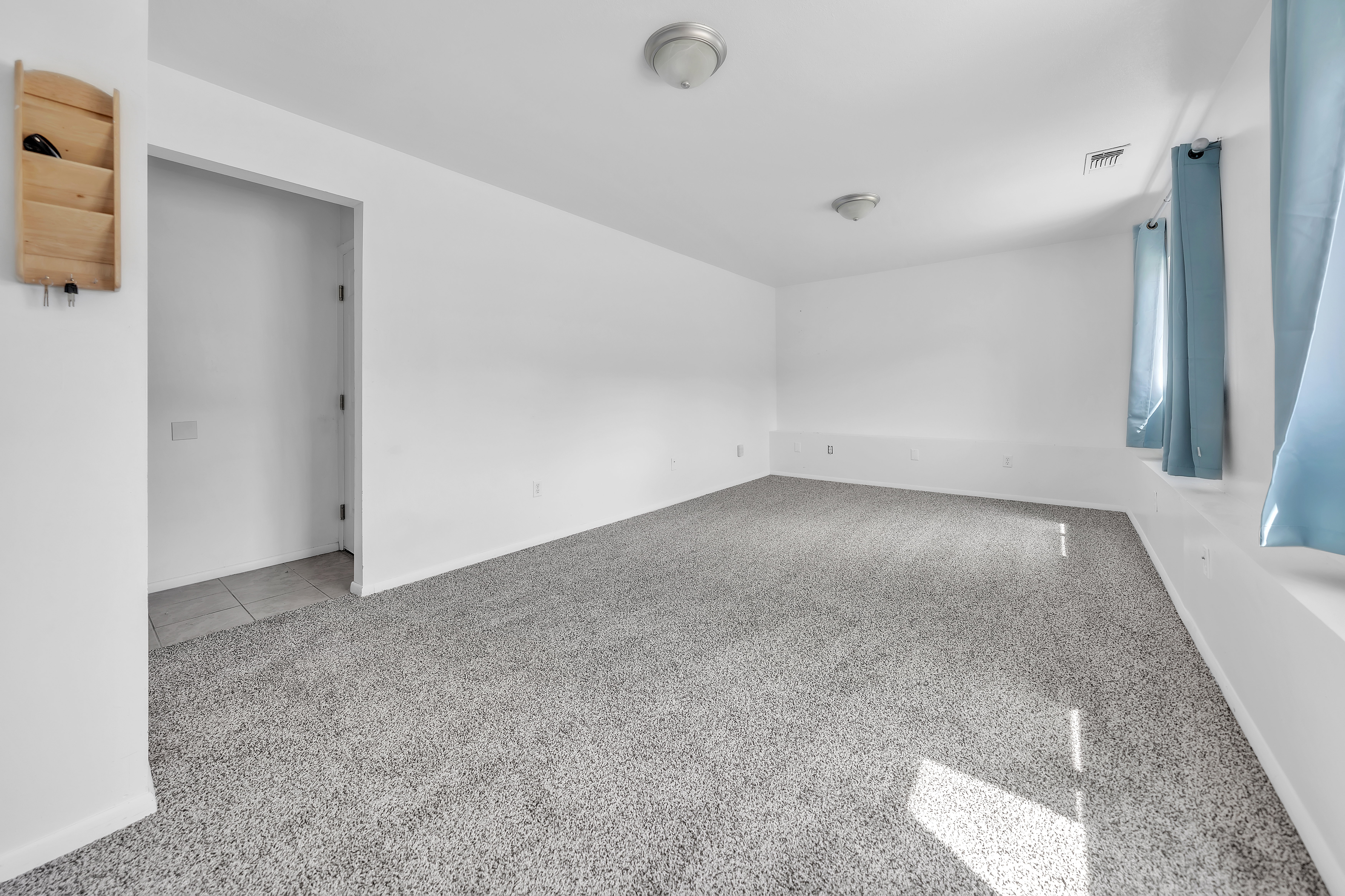 Spacious interior room featuring light gray carpeting, white walls, and two ceiling-mounted dome light fixtures
