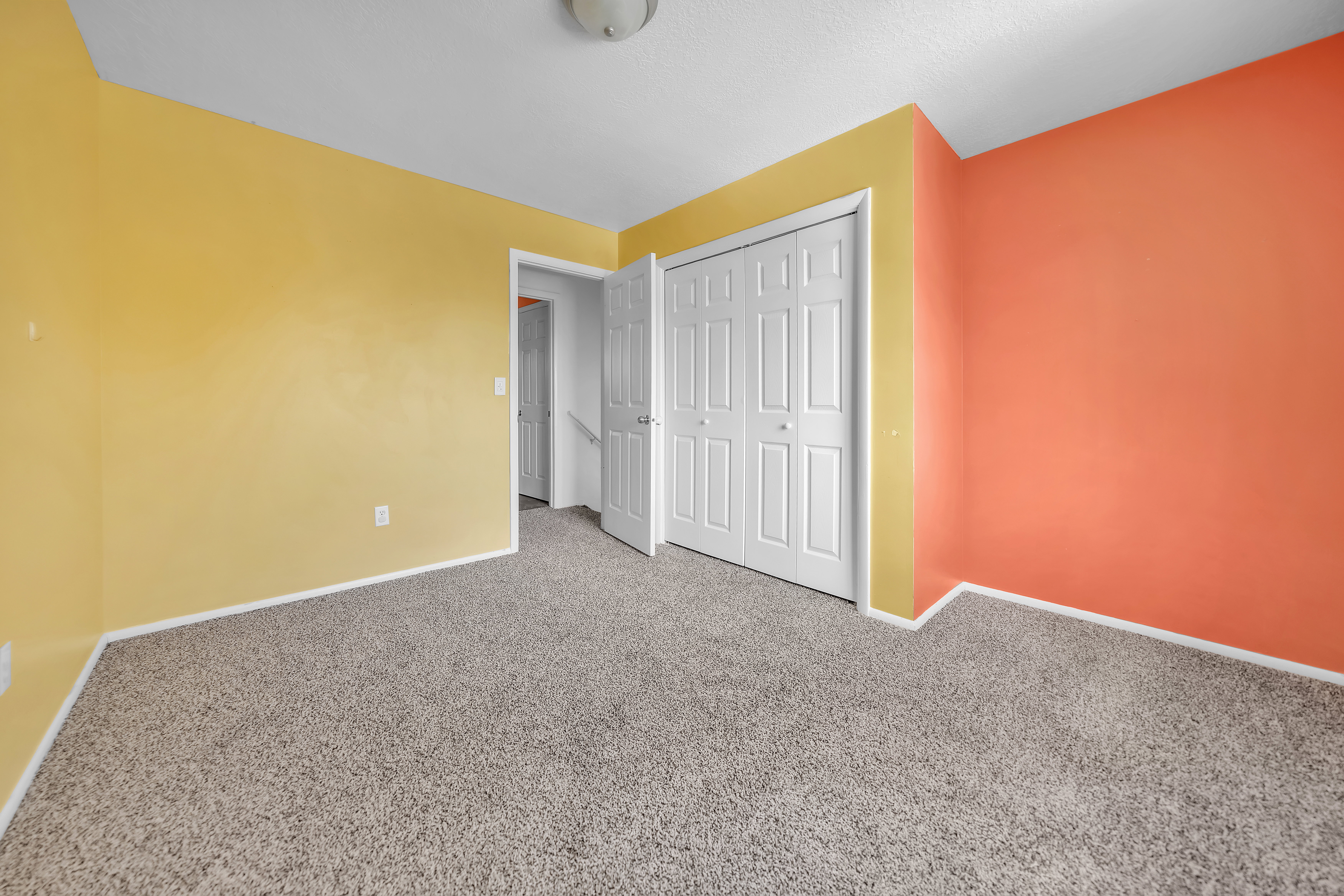 Carpeted interior space featuring bright yellow and orange walls, white trim, and a white bi-fold closet