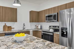 Kitchen with stainless steel appliances, light stone counters, wood finish cabinets, modern cabinets, and backsplash