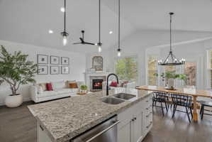 Kitchen with a stone fireplace, an island with sink, white cabinets, dark wood finished floors, and vaulted ceiling