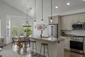 Kitchen featuring stainless steel appliances, a breakfast bar area, decorative backsplash, dark wood-style floors, and a center island with sink