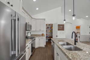 Kitchen with stainless steel appliances, lofted ceiling, dark wood-style floors, hanging light fixtures, and white cabinets