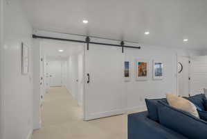 Living area featuring a barn door, recessed lighting, and light carpet