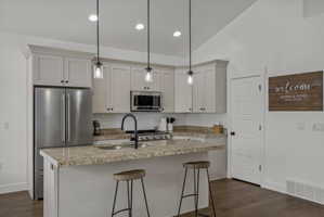 Kitchen with stainless steel appliances, a center island with sink, a kitchen breakfast bar, light stone countertops, and vaulted ceiling