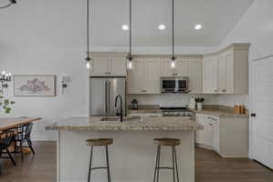 Kitchen featuring hanging light fixtures, dark wood-style flooring, lofted ceiling, a breakfast bar, and light stone counters