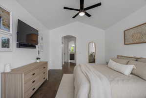 Bedroom with arched walkways, dark wood finished floors, a ceiling fan, vaulted ceiling, and connected bathroom