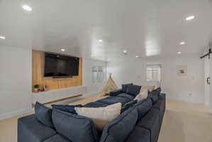 Living area featuring a barn door, light colored carpet, and recessed lighting