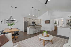 Living area with arched walkways, vaulted ceiling, dark wood-type flooring, and suspended lighting