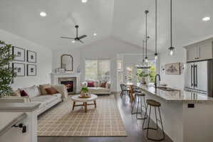 Living room featuring dark wood-type flooring, a stone fireplace, a ceiling fan, and recessed lighting