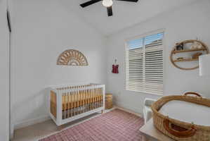 Bedroom featuring a nursery area, vaulted ceiling, light carpet, and ceiling fan