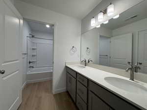 Full bathroom featuring double vanity, washtub / shower combination, light wood-style floors, and a textured ceiling