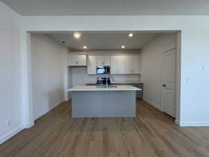 Dual tone kitchen featuring recessed lighting, light wood-style floors, a kitchen island with sink, stainless steel appliances, and light stone counters