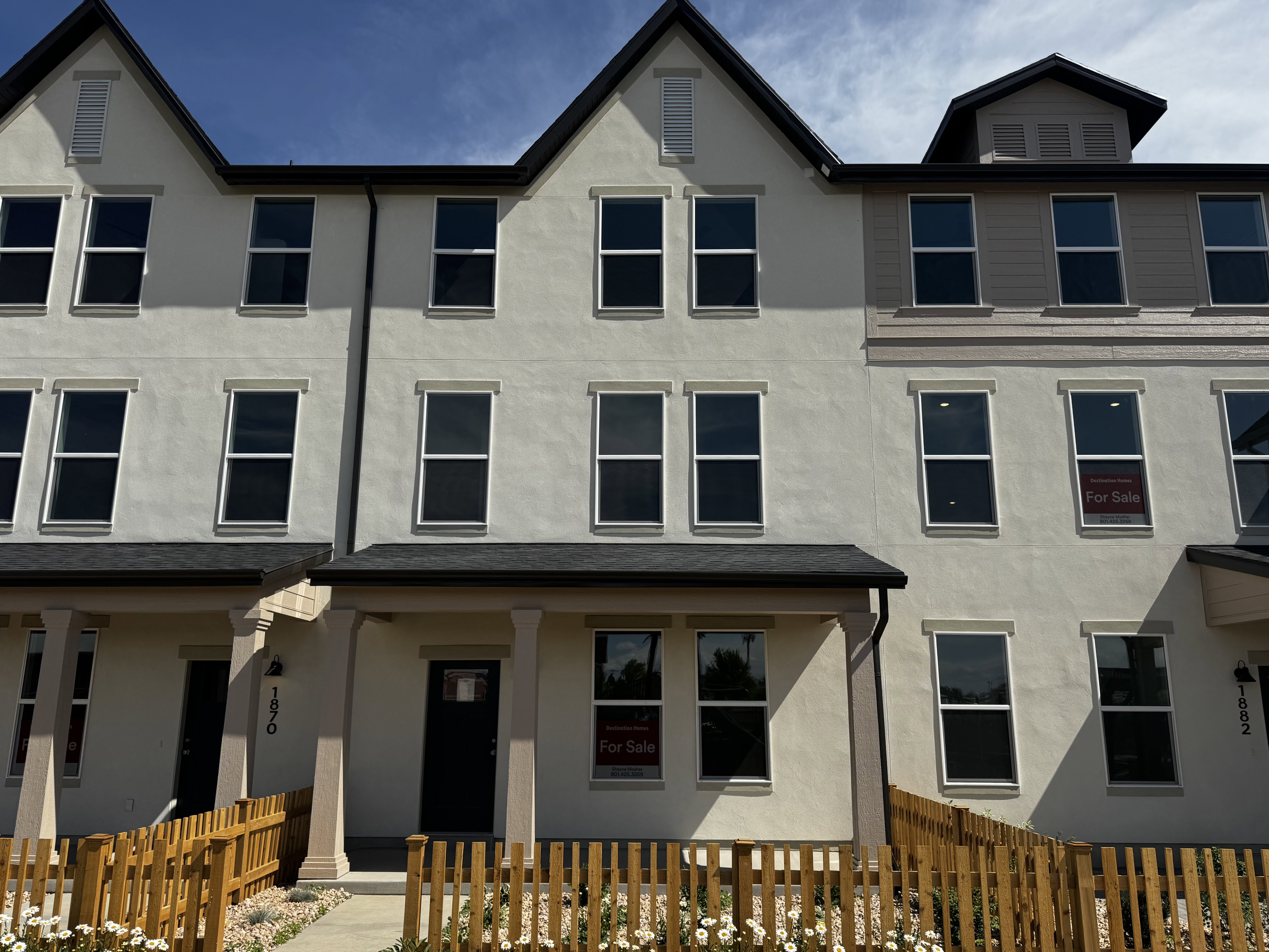 Modern townhome featuring a neutral stucco exterior, dark roofline, and multiple vertical windows