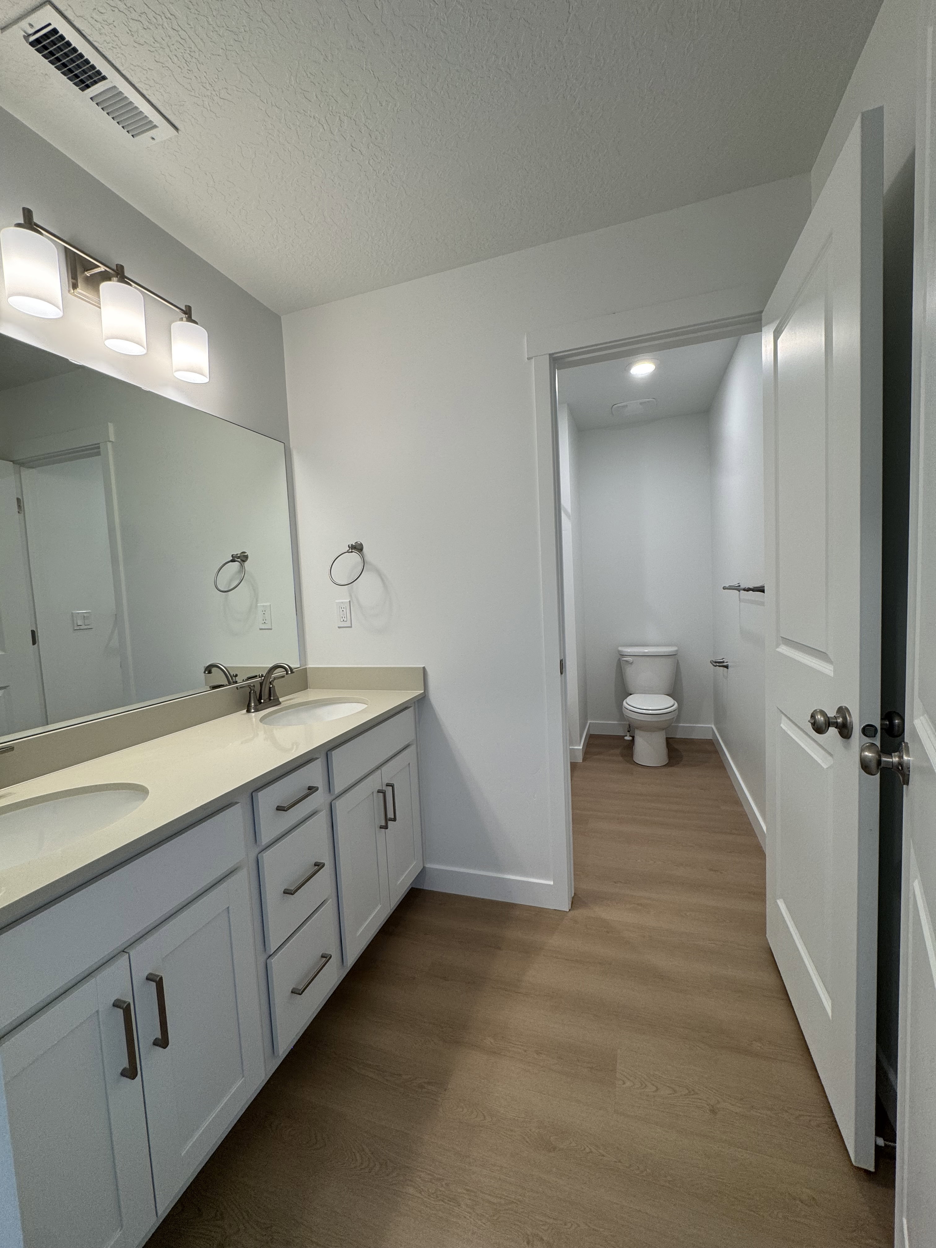 Full bathroom featuring double vanity, dark wood finished floors, and a textured ceiling