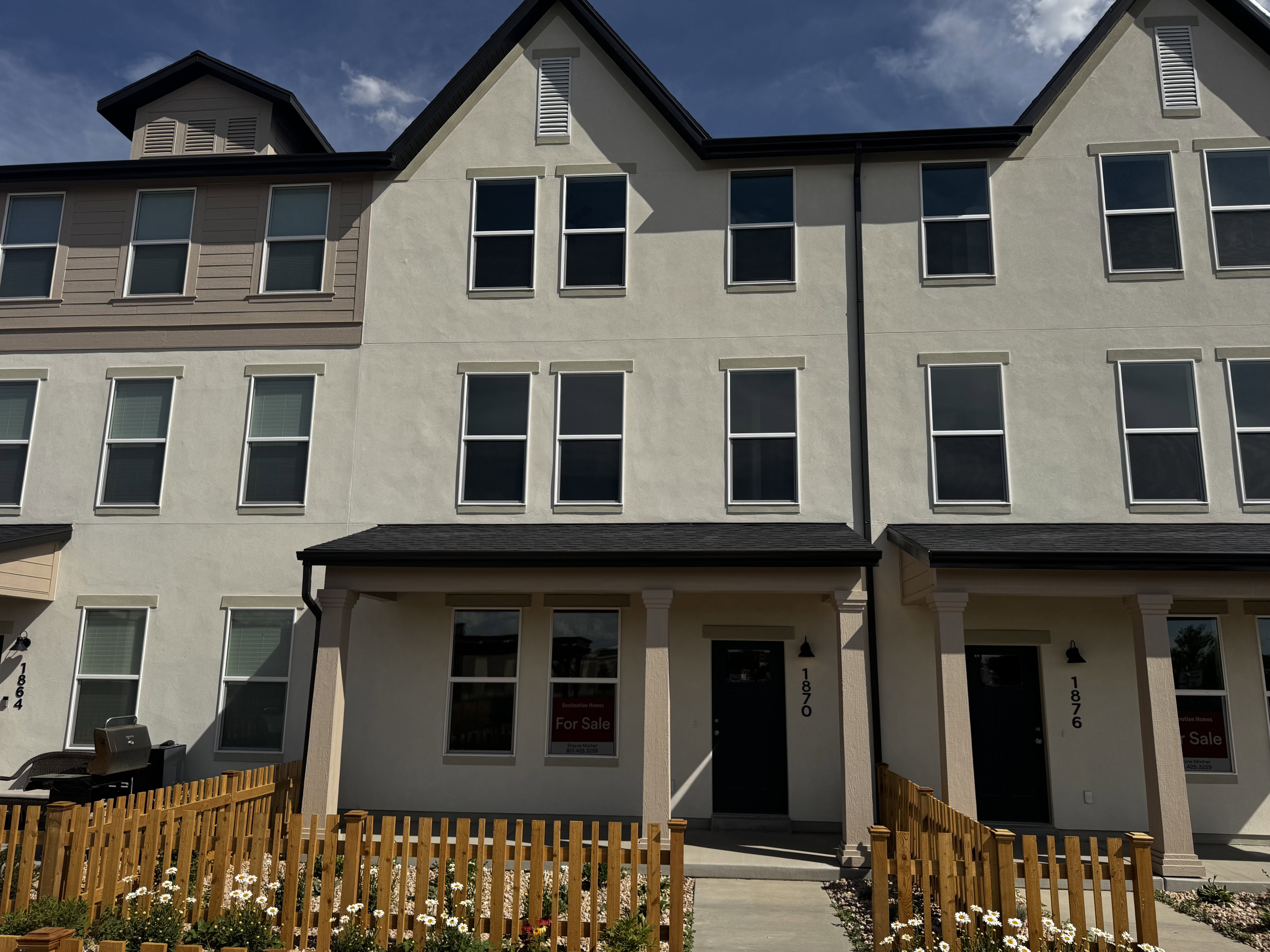 Multi-story townhome with light-toned stucco exterior, dark trim, and a gabled roofline