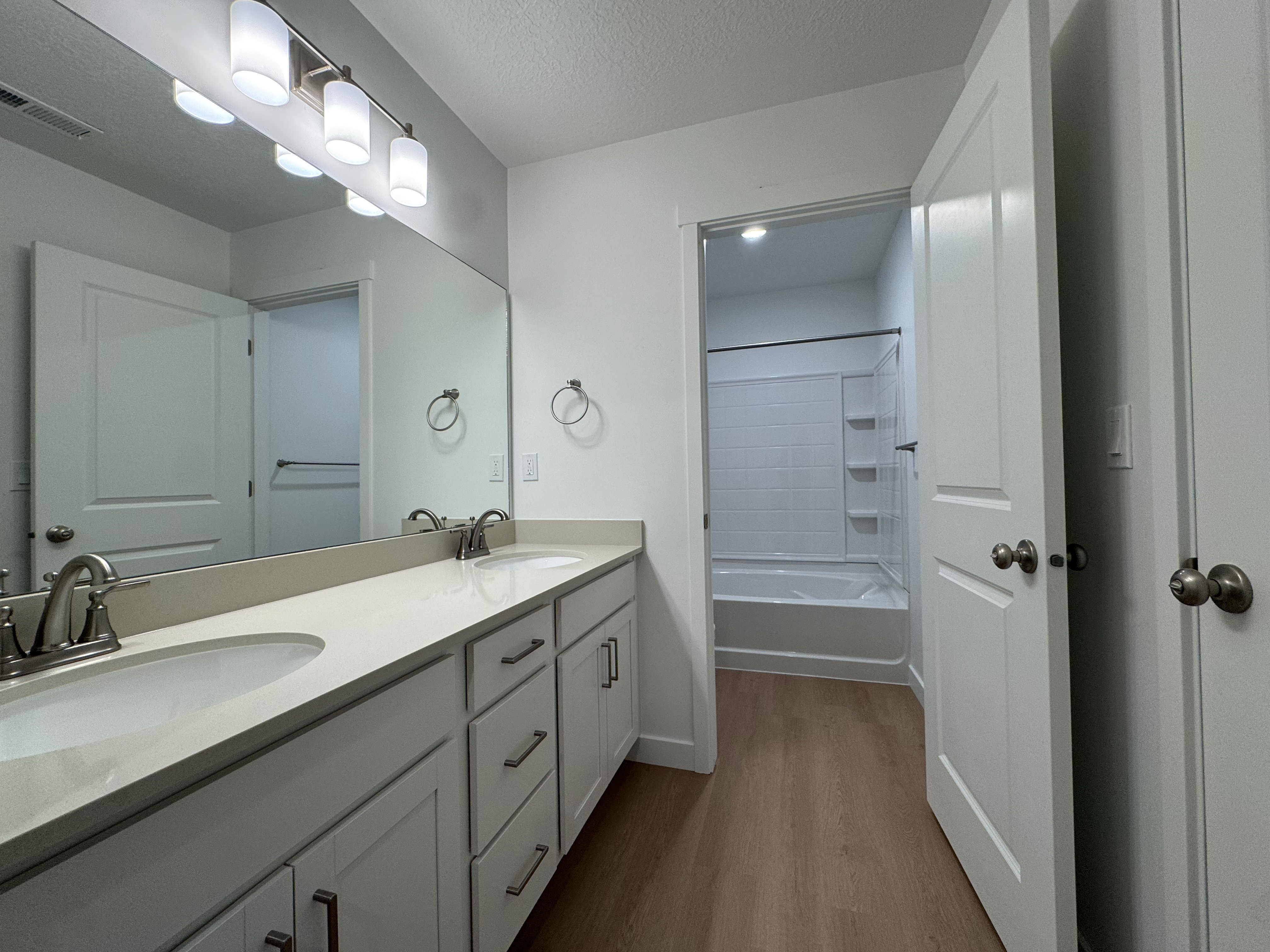 Full bathroom with double vanity, tub / shower combination, dark wood-type flooring, and a textured ceiling