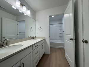 Full bathroom with double vanity, tub / shower combination, dark wood-type flooring, and a textured ceiling