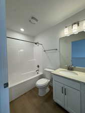 Bathroom with vanity, dark wood-type flooring, shower / bath combination, and a textured ceiling