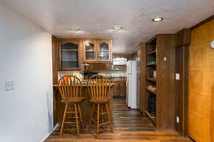 Kitchen with wood finish cabinetry, dark wood-style floors, glass insert cabinets, freestanding refrigerator, and open shelves