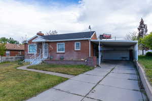 View of front of home with concrete driveway, a garage, brick siding, a chimney, and a carport