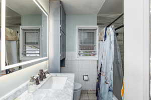 Bathroom featuring vanity, tile walls, wainscoting, plenty of natural light, and light tile patterned floors