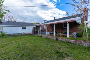 Back of house featuring a lawn, a patio, brick siding, and a chimney