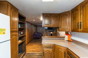 Kitchen featuring freestanding refrigerator, wood finish cabinetry, open shelves, a textured ceiling, and dark wood-style floors