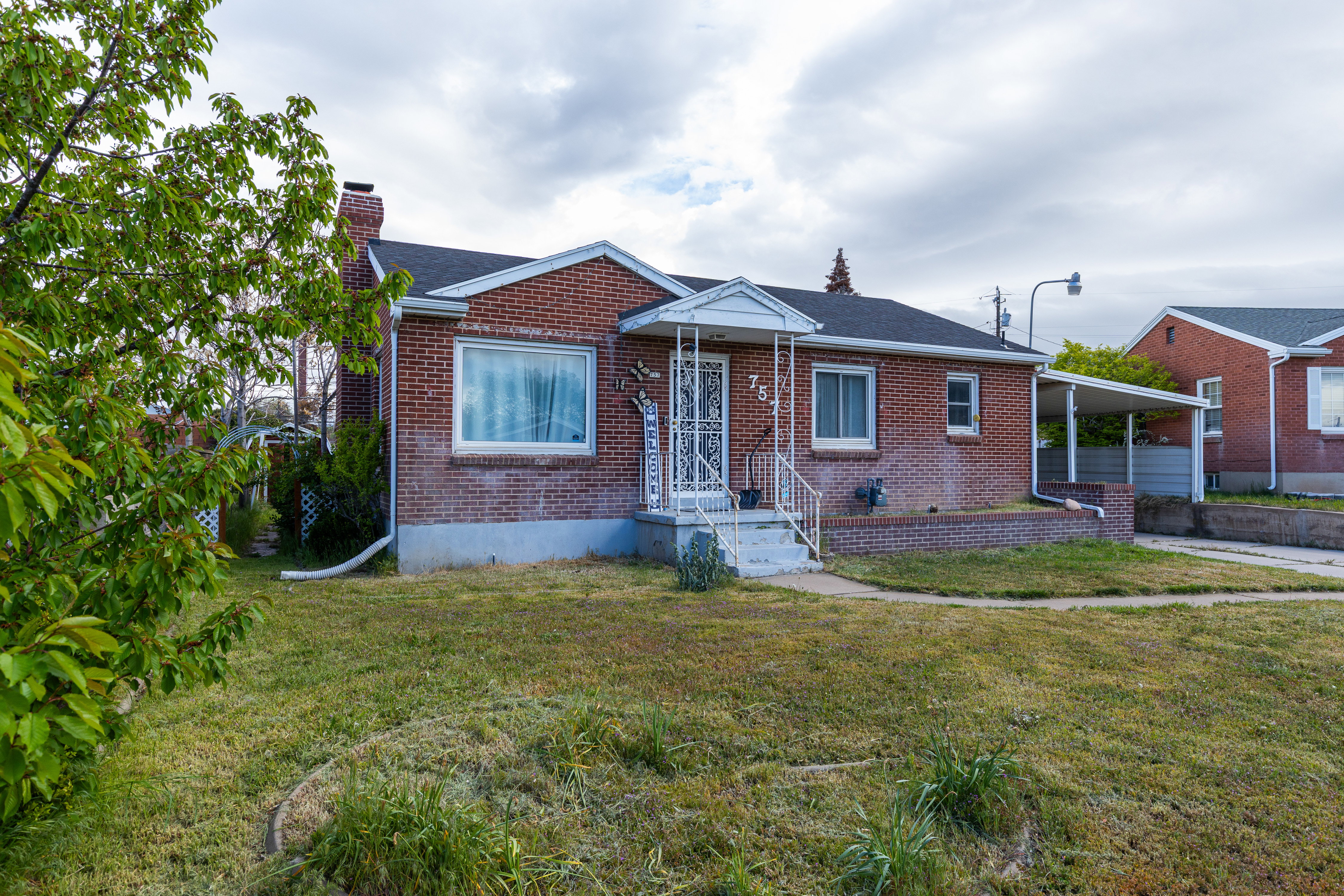 Bungalow-style house with a front yard, brick siding, a chimney, a carport, and a shingled roof