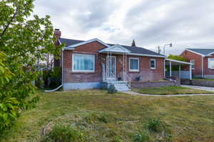 Bungalow-style house with a front yard, brick siding, a chimney, a carport, and a shingled roof