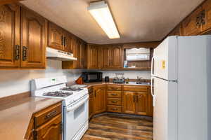 Kitchen featuring white appliances, wood finish cabinetry, a textured ceiling, and dark wood-style floors