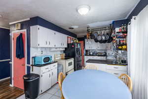 Kitchen featuring dark countertops, white cabinetry, white range with electric cooktop, a textured ceiling, and a textured wall
