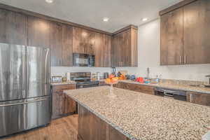 Kitchen with black appliances, dark wood finish cabinetry, light stone counters, light wood-type flooring, and recessed lighting