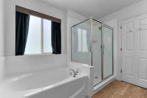 Full bath with a stall shower, a bath, and light wood finished floors