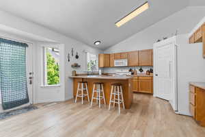 Kitchen with a breakfast bar area, white appliances, vaulted ceiling, a peninsula, and light countertops