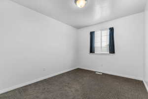 Unfurnished room with dark carpet and baseboards