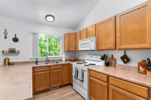 Kitchen featuring white appliances, light countertops, lofted ceiling, light wood-style flooring, and wood finish cabinets