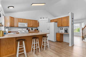 Kitchen with light countertops, white appliances, wood finish cabinetry, a peninsula, and a breakfast bar