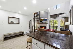 Kitchen with open floor plan, a stone fireplace, light wood finished floors, a kitchen breakfast bar, and white cabinets