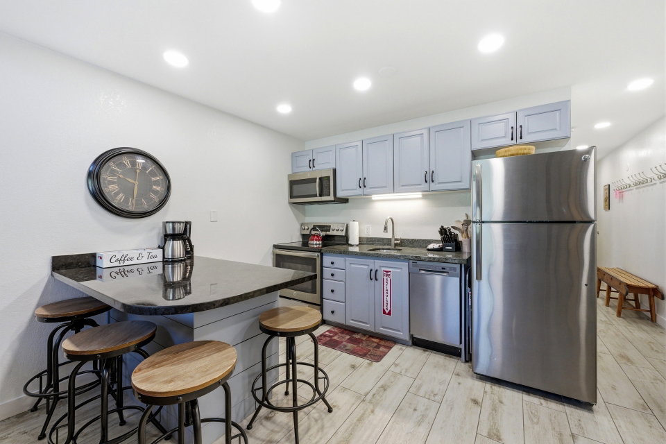 Kitchen with a kitchen bar, stainless steel appliances, light wood-style flooring, dark stone countertops, and recessed lighting