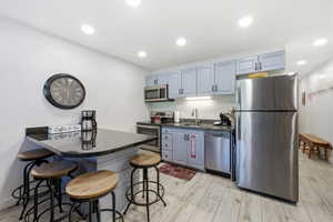 Kitchen with a kitchen bar, stainless steel appliances, light wood-style flooring, dark stone countertops, and recessed lighting