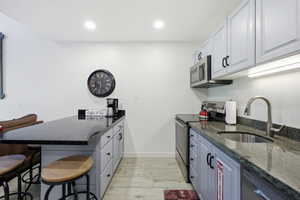 Kitchen with a peninsula, a breakfast bar area, dark stone counters, stainless steel appliances, and recessed lighting