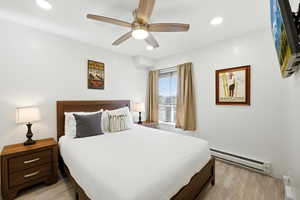 Bedroom with baseboard heating, light wood-style flooring, ceiling fan, and recessed lighting