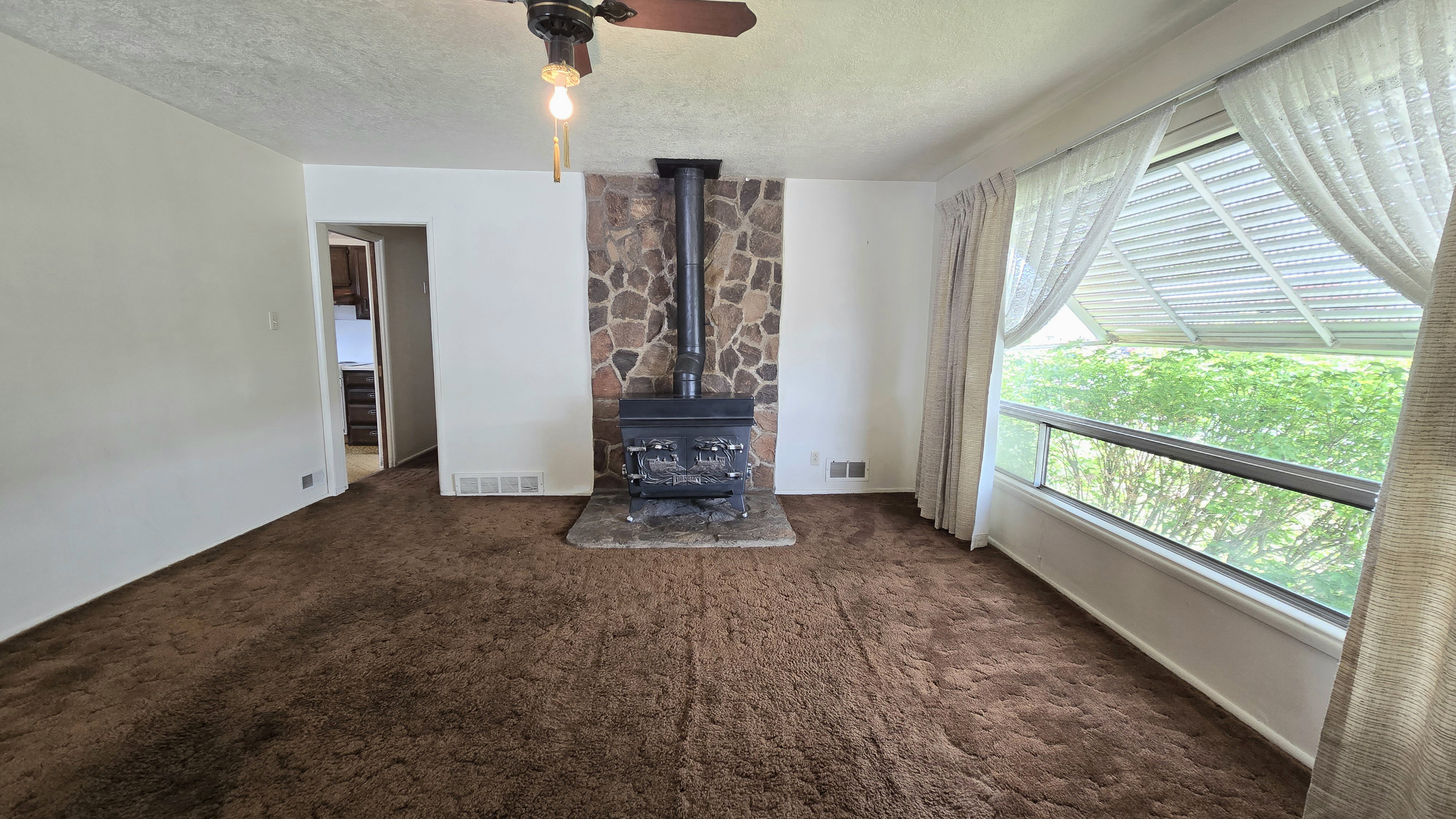 Living room featuring ceiling fan, a textured ceiling, a wood stove, and dark colored carpet