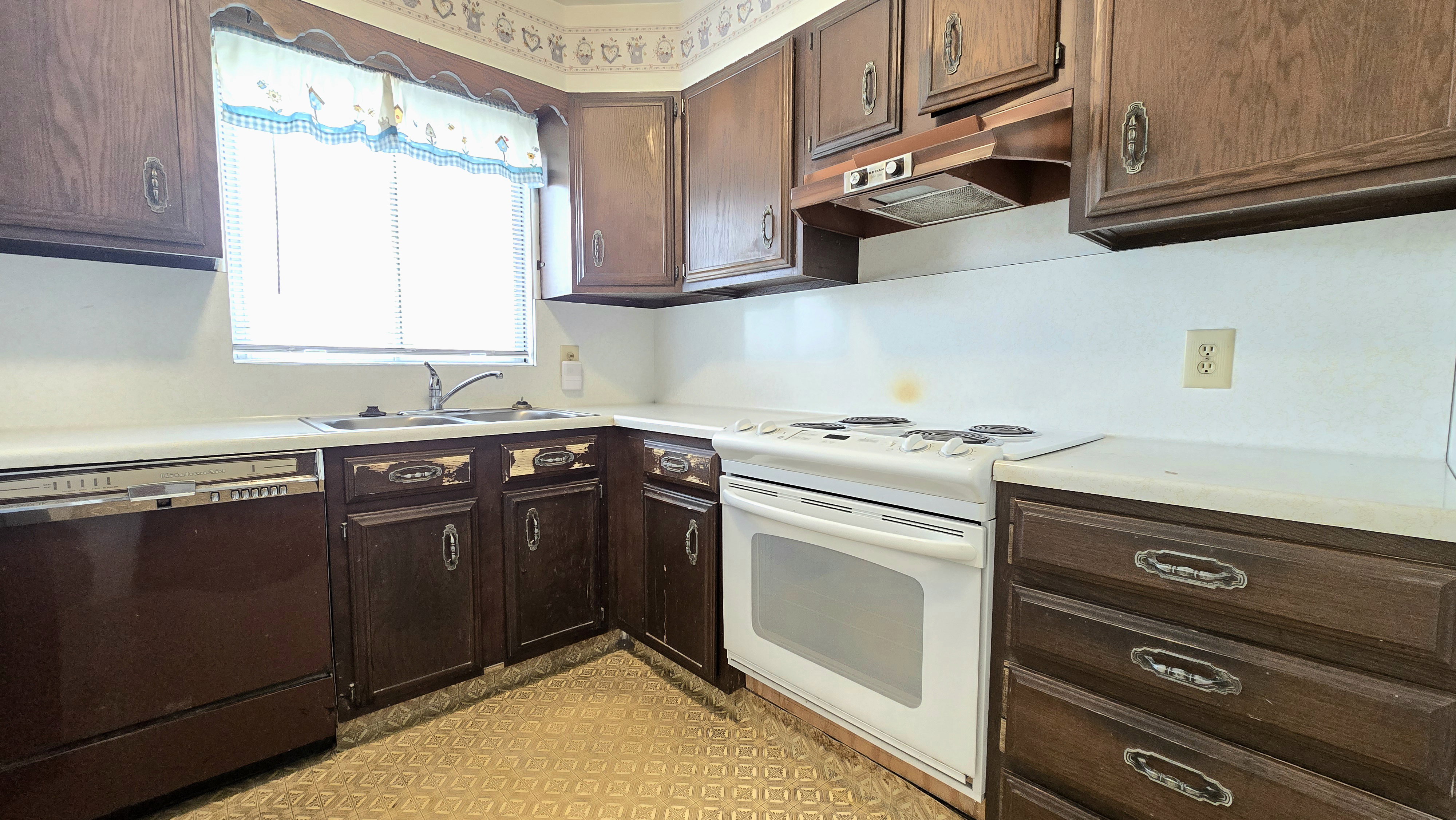 Kitchen with white electric range, light countertops, dishwashing machine, dark wood finish cabinets, and light flooring