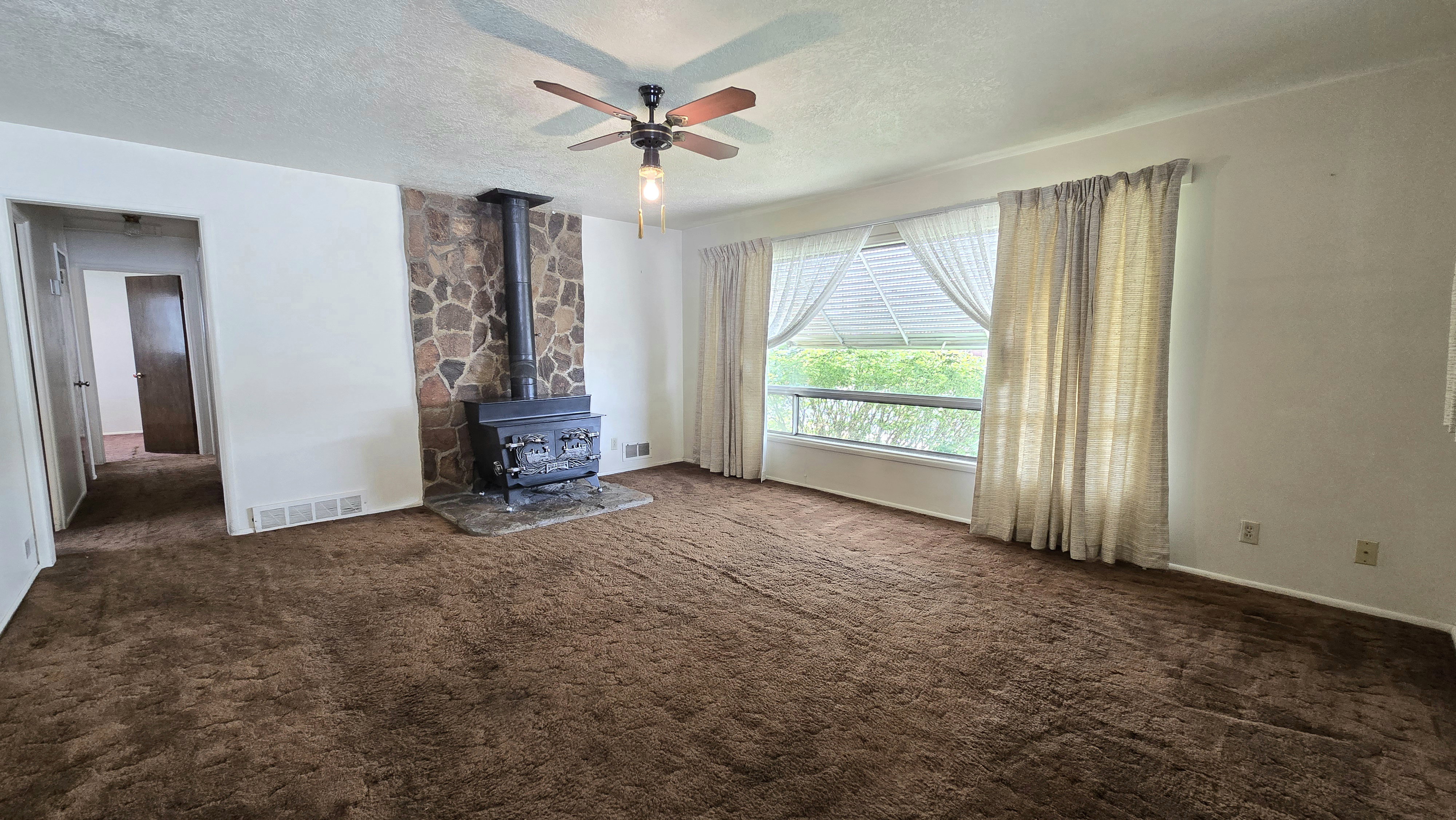 Unfurnished living room with a textured ceiling, a wood stove, ceiling fan, and dark carpet