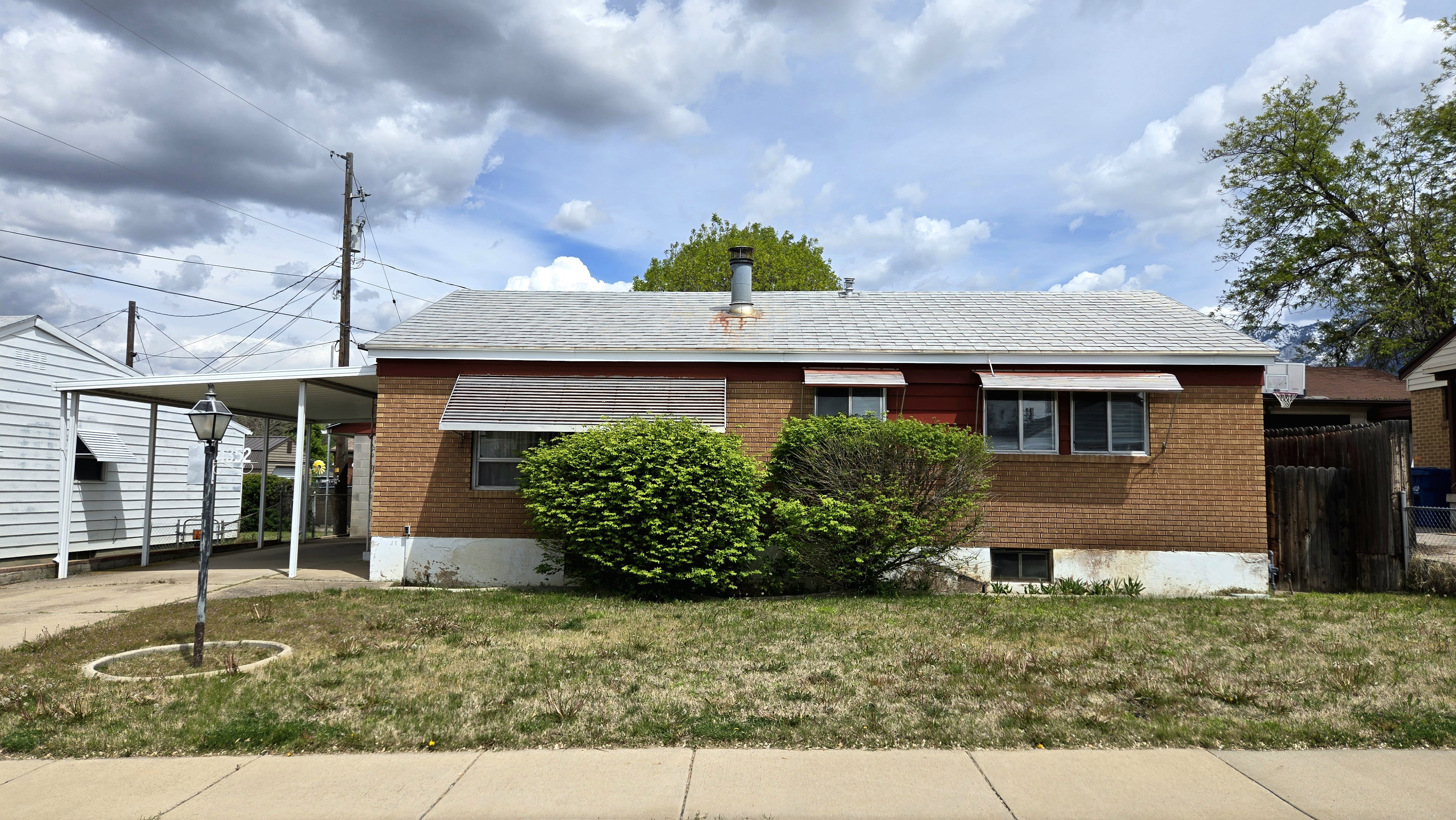 View of property exterior featuring a lawn, a carport, brick siding, and concrete driveway