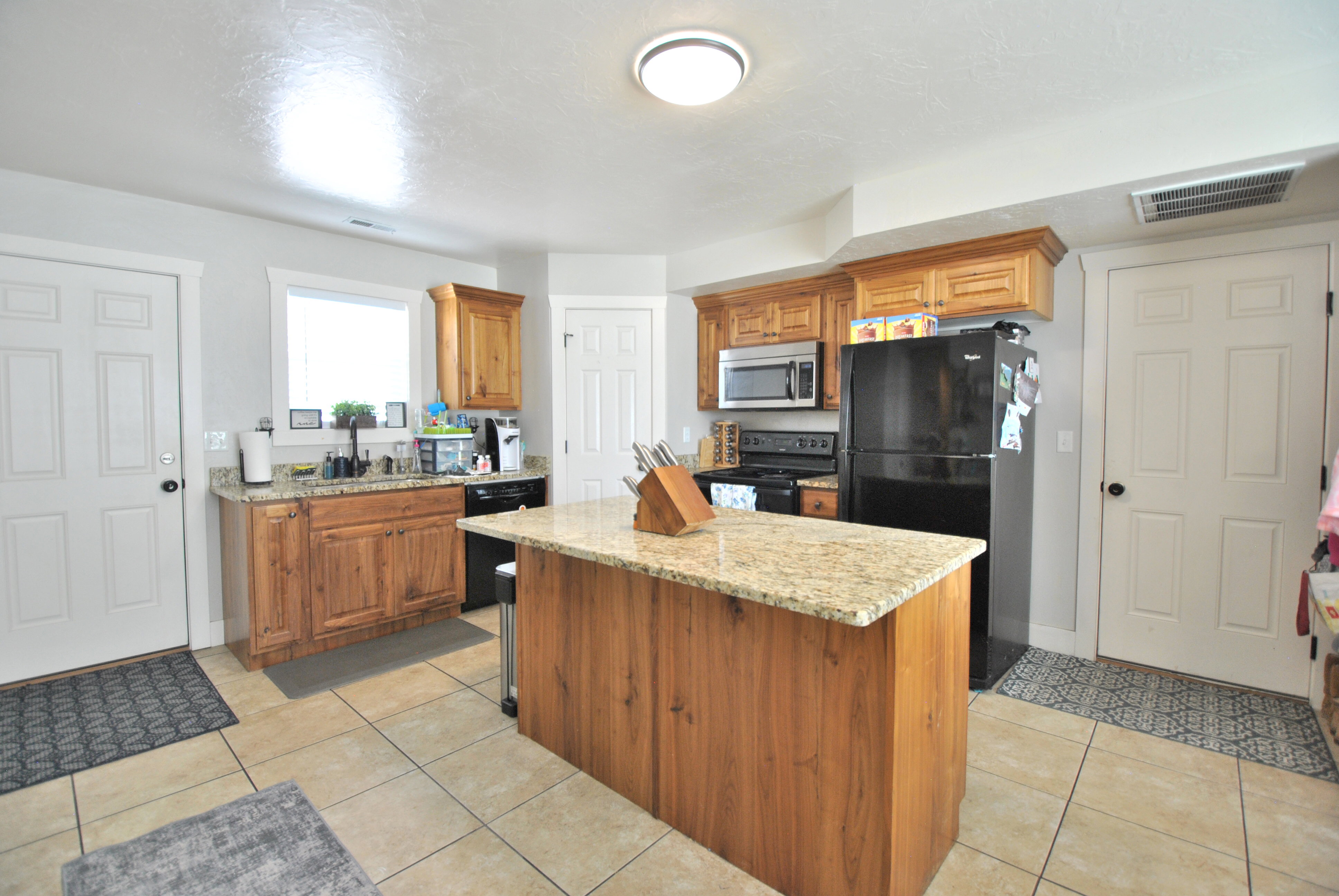 Kitchen featuring wood finish cabinetry, a center island, black appliances, light stone counters, and light tile patterned flooring