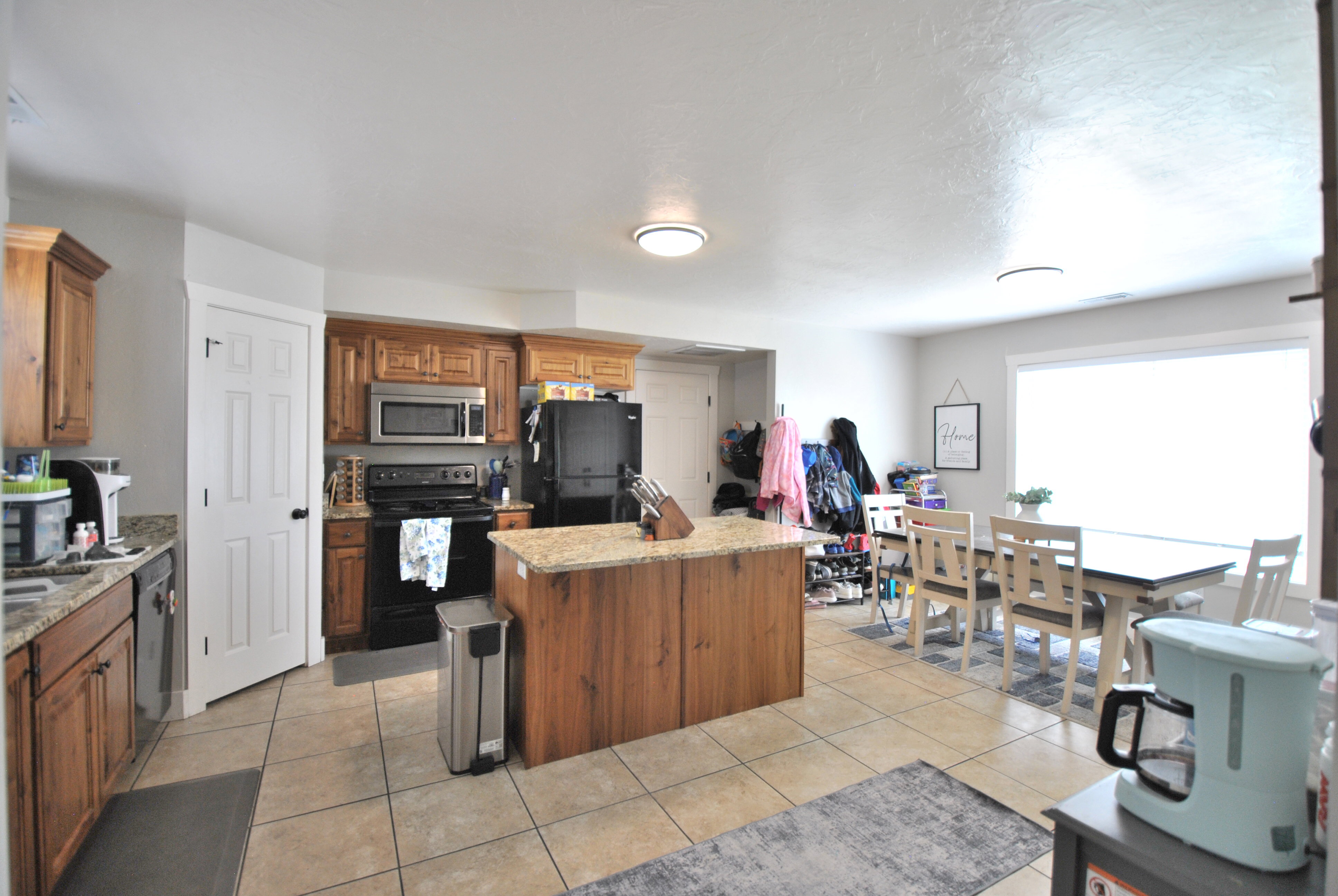 Kitchen with black appliances, a center island, wood finish cabinets, light stone countertops, and light tile patterned flooring