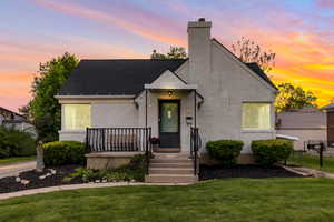 View of front of house featuring a yard, a chimney, brick siding, and roof with shingles