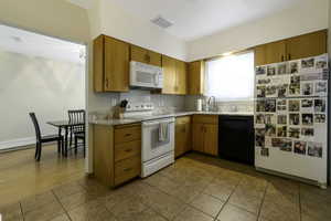 Kitchen featuring white appliances, light stone countertops, wood finish cabinets, and light tile patterned flooring